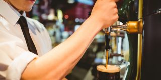 Cropped image of bartender holding beer glass below dispenser ta